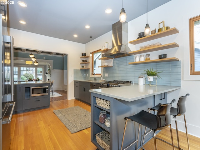 kitchen with hanging light fixtures, a peninsula, island range hood, and open shelves