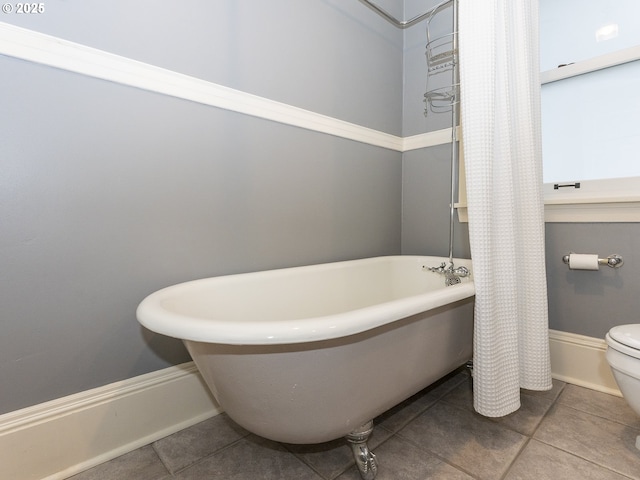 full bath featuring tile patterned flooring, a freestanding tub, baseboards, and toilet