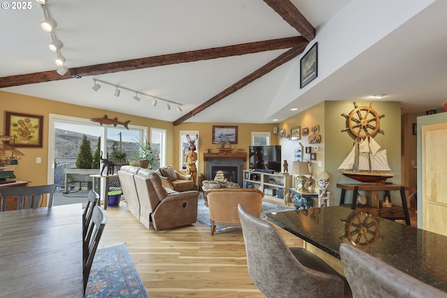 dining area with light wood-style floors, a fireplace, and lofted ceiling with beams