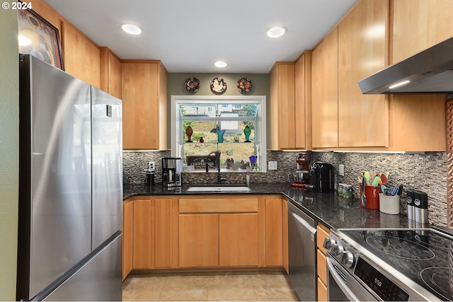 kitchen with backsplash, appliances with stainless steel finishes, a sink, dark stone countertops, and wall chimney exhaust hood