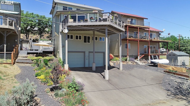 back of house with driveway, an attached garage, stairs, and a storage unit