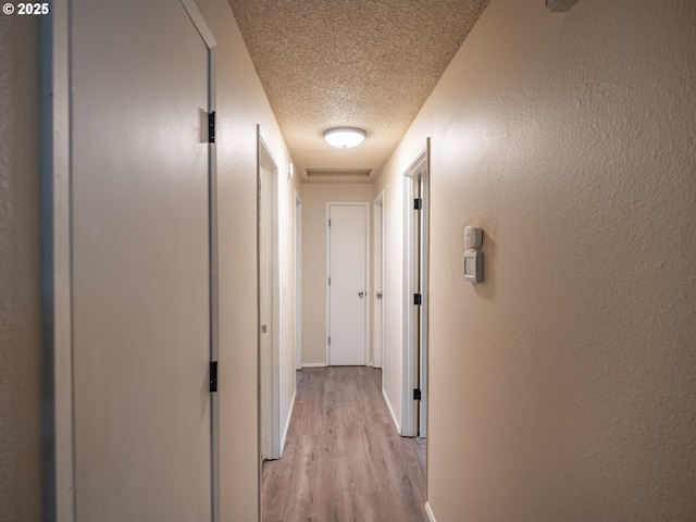 hall with a textured ceiling and light wood-type flooring