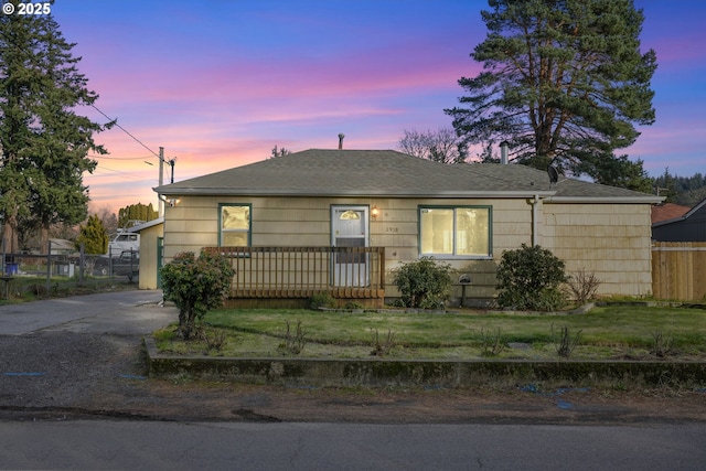 view of front of home featuring driveway, a shingled roof, fence, and a yard