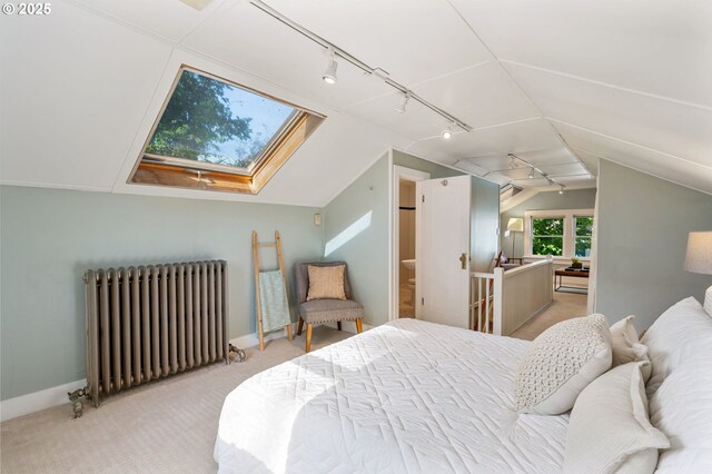 bedroom featuring vaulted ceiling with skylight, light colored carpet, rail lighting, baseboards, and radiator