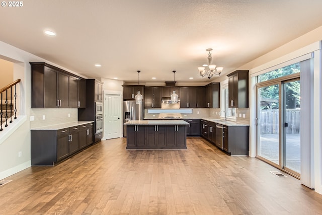 kitchen featuring pendant lighting, light hardwood / wood-style flooring, appliances with stainless steel finishes, a center island, and dark brown cabinetry