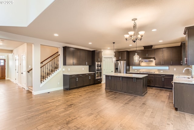 kitchen with appliances with stainless steel finishes, a center island, dark brown cabinets, and decorative light fixtures