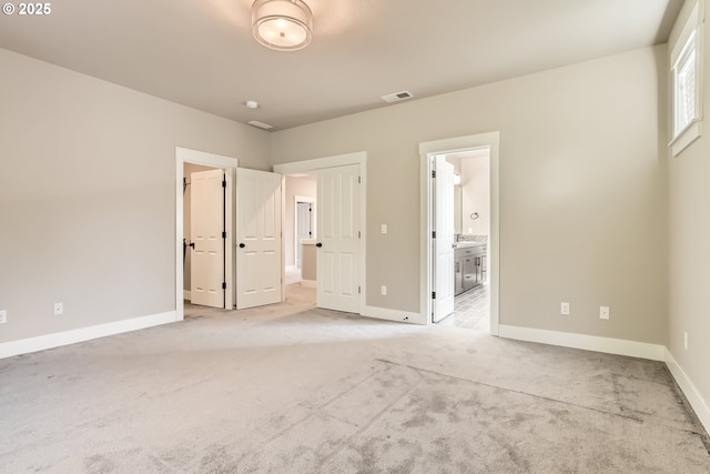 unfurnished bedroom featuring ensuite bathroom and light carpet