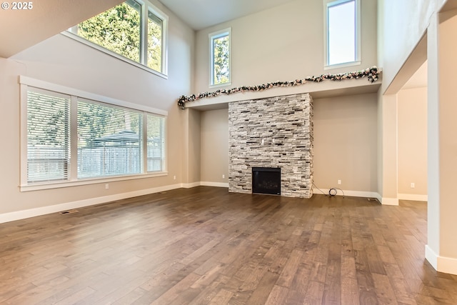 unfurnished living room with a high ceiling, wood-type flooring, and a stone fireplace