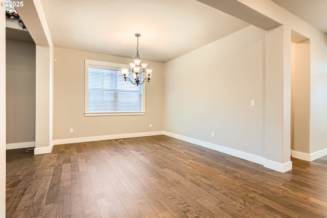 spare room featuring dark wood-type flooring and a chandelier