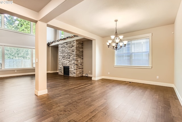 unfurnished living room featuring an inviting chandelier, a stone fireplace, and dark wood-type flooring