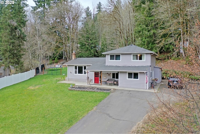 split level home with a patio, fence, driveway, a chimney, and a front lawn