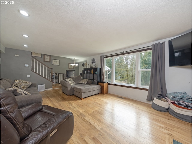 living area featuring light wood-type flooring, visible vents, a textured ceiling, an inviting chandelier, and stairs