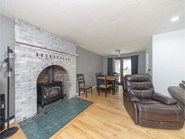 living area with a wood stove, wood finished floors, baseboards, and a textured ceiling