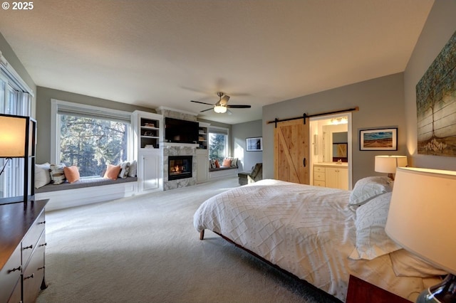 carpeted bedroom with ceiling fan, multiple windows, a tile fireplace, and a barn door