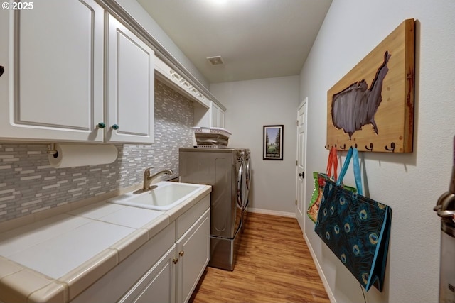 washroom with washer and clothes dryer, sink, light hardwood / wood-style floors, and cabinets