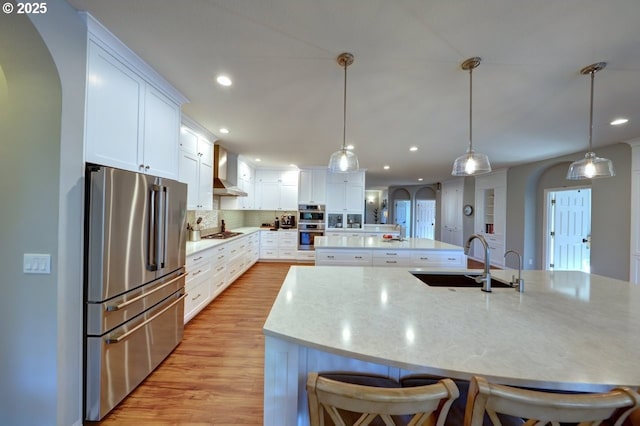 kitchen with white cabinets, appliances with stainless steel finishes, decorative light fixtures, wall chimney range hood, and sink