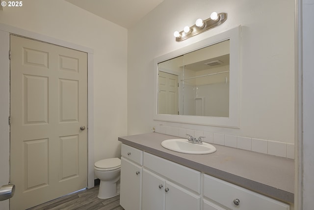 bathroom with hardwood / wood-style flooring, vanity, walk in shower, and toilet