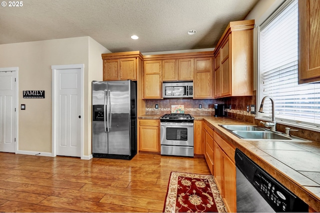 12626 Tradewind St, Oregon City, OR 97045 - kitchen featuring stainless steel appliances, a sink, tile countertops, light wood-style flooring, and tasteful backsplash