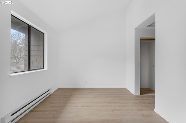 spare room featuring light hardwood / wood-style flooring, lofted ceiling, and a baseboard heating unit