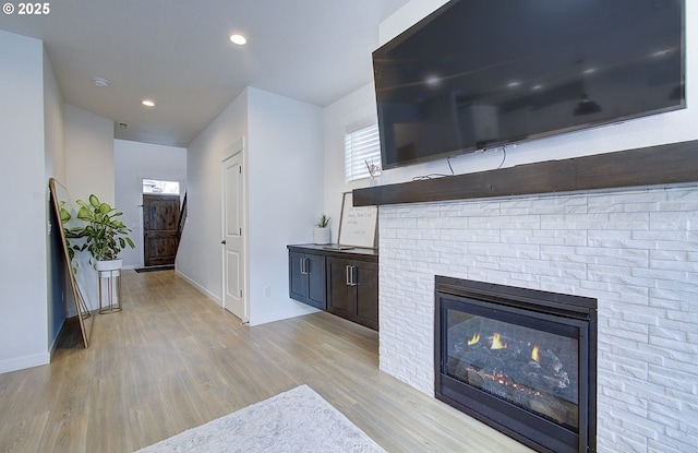unfurnished living room featuring recessed lighting, a stone fireplace, light wood finished floors, and baseboards
