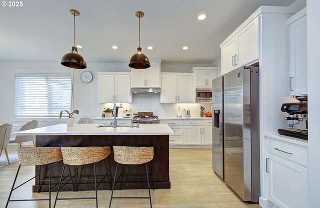 kitchen with under cabinet range hood, appliances with stainless steel finishes, a kitchen bar, and white cabinetry