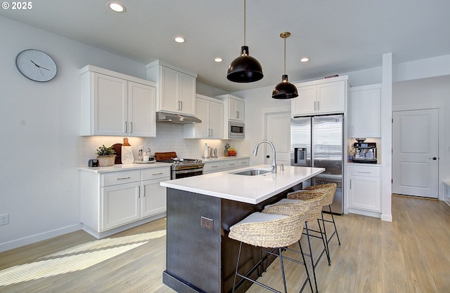 kitchen with a sink, a breakfast bar area, appliances with stainless steel finishes, light wood-style flooring, and under cabinet range hood