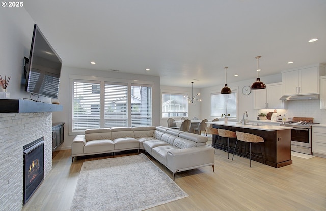 living area featuring recessed lighting, a stone fireplace, and light wood-style flooring