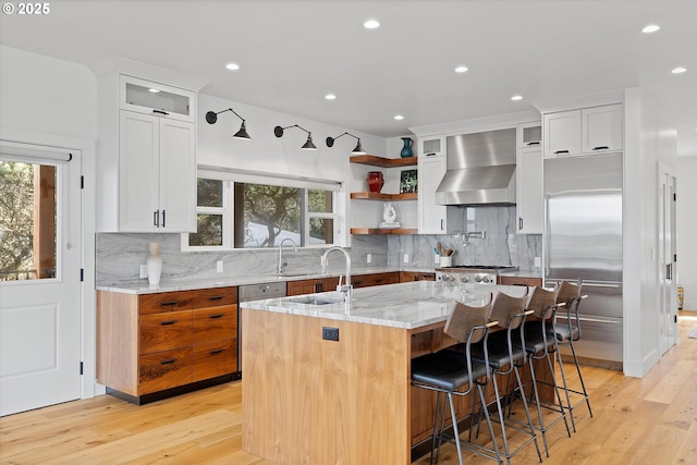 kitchen featuring wall chimney range hood, light wood finished floors, stainless steel appliances, and a sink