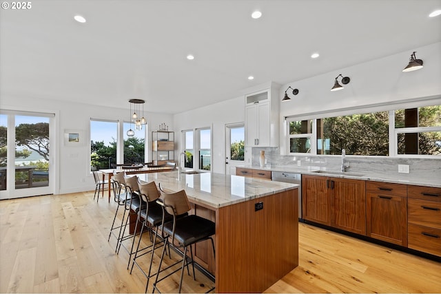 kitchen with a sink, light wood-style floors, light stone counters, and dishwasher