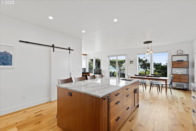8466 NW Coast Rd, Seal Rock, OR 97376 - kitchen with a barn door, a sink, light wood-style flooring, light stone counters, and an island with sink