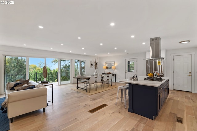 kitchen featuring a breakfast bar area, gas cooktop, stainless steel fridge, a kitchen island with sink, and light hardwood / wood-style floors