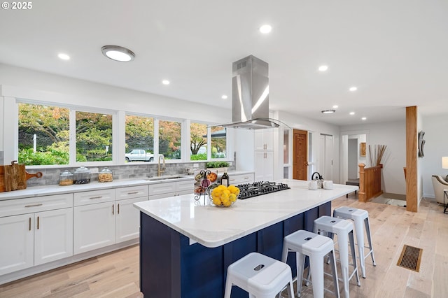 kitchen featuring white cabinetry, island range hood, light stone counters, and a kitchen island