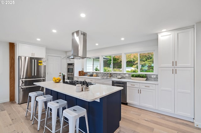 kitchen with a breakfast bar, white cabinetry, a center island, appliances with stainless steel finishes, and island exhaust hood