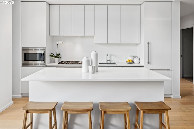 kitchen with light countertops, stainless steel microwave, white cabinetry, an island with sink, and modern cabinets