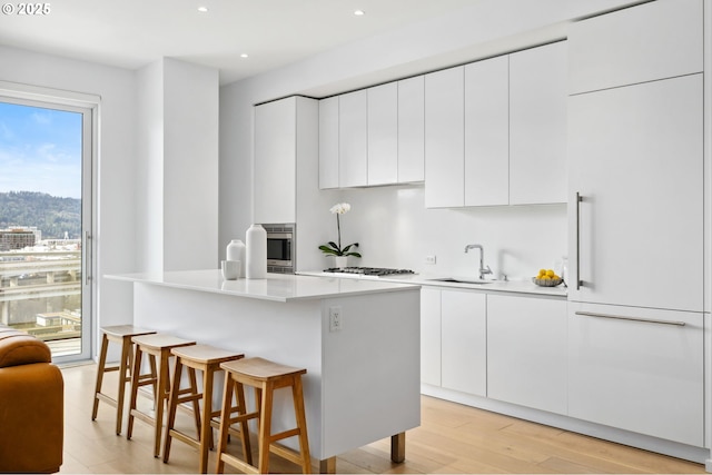 kitchen with white cabinets, a kitchen island, light countertops, and a sink