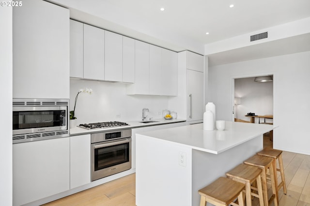 kitchen featuring white cabinets, modern cabinets, a breakfast bar area, stainless steel appliances, and light countertops