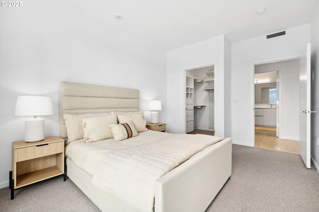 bedroom featuring a walk in closet, a closet, light colored carpet, visible vents, and baseboards