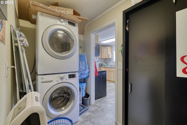 clothes washing area with stacked washer and dryer, crown molding, and laundry area