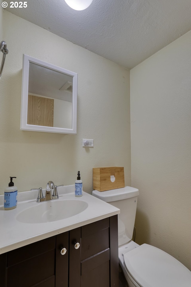 bathroom with a textured ceiling, vanity, and toilet