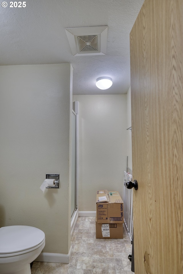 bathroom featuring a shower stall, stone finish flooring, toilet, baseboards, and a textured ceiling