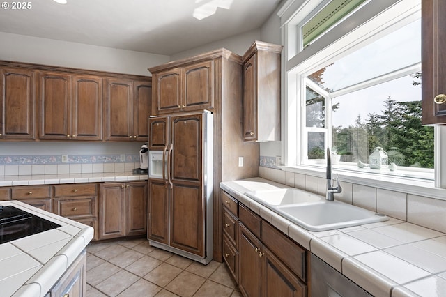 kitchen with paneled refrigerator, tile counters, light tile patterned flooring, and a sink