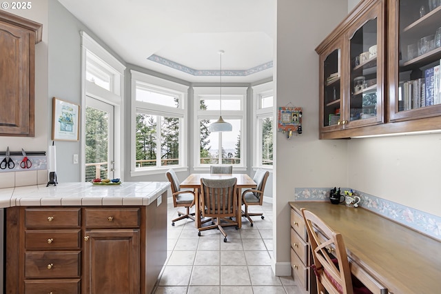 kitchen featuring glass insert cabinets, tile counters, hanging light fixtures, a peninsula, and light tile patterned flooring