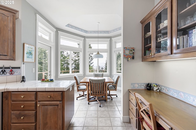 kitchen featuring glass insert cabinets, light tile patterned flooring, a tray ceiling, and a peninsula