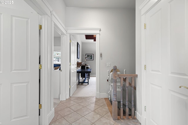 hallway featuring an upstairs landing, light tile patterned flooring, light colored carpet, and baseboards