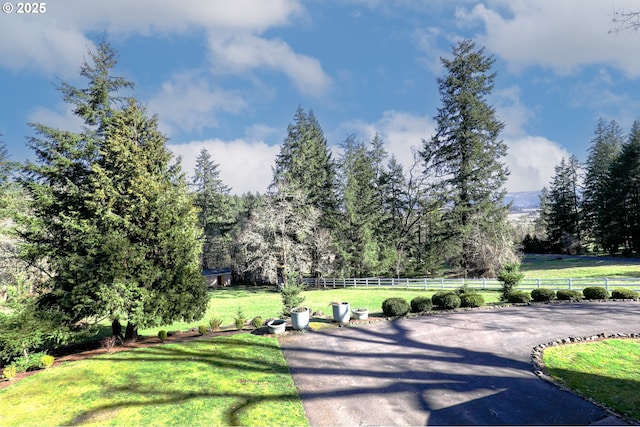 surrounding community with a rural view, a lawn, and fence