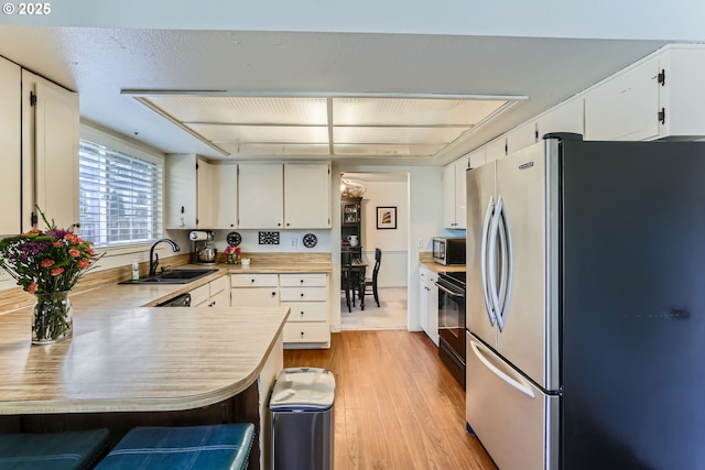 kitchen featuring sink, white cabinets, kitchen peninsula, and appliances with stainless steel finishes