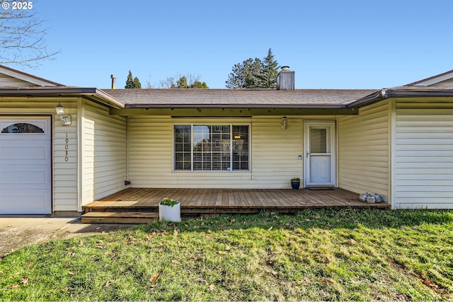 view of exterior entry with a garage, a wooden deck, and a yard