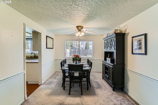 dining area with sink, ceiling fan, dark colored carpet, and a textured ceiling