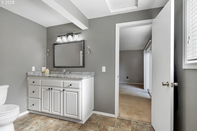 half bathroom with toilet, stone finish floor, baseboards, and vanity