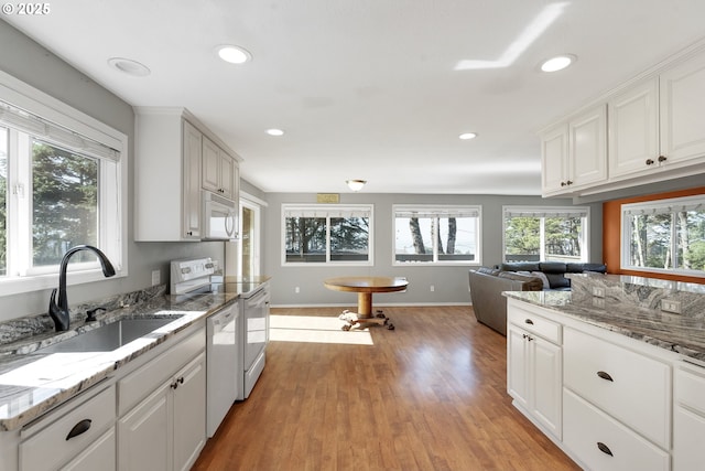 kitchen featuring white appliances, light wood-type flooring, white cabinetry, a sink, and recessed lighting